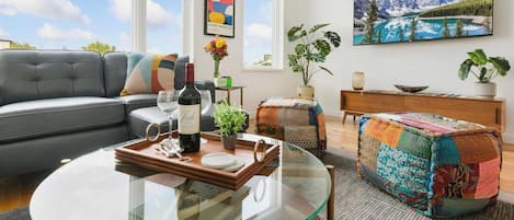 A modern living room with a sofa, coffee table, and a painting of a mountain landscape.