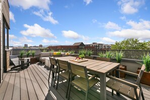 A wooden deck with a table and chairs, potted plants, and a view of buildings in the background. - The Overlook - Luxe Old Town Condo w/ King Suite (Fort Collins)