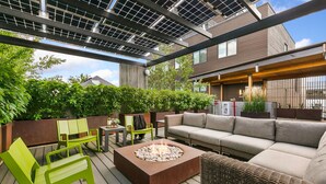 An outdoor patio area with a fire pit, green and grey seating, and a modern building in the background. - The Overlook - Luxe Old Town Condo w/ King Suite (Fort Collins)