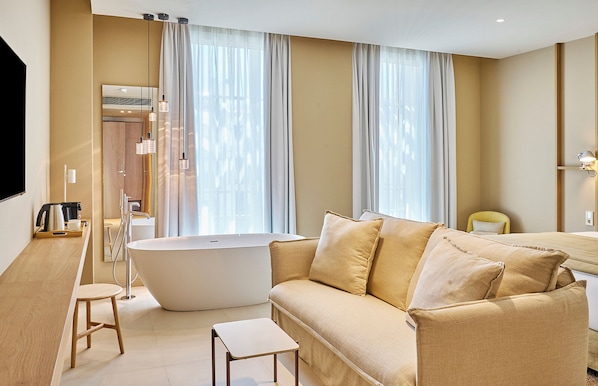 A modern bathroom with a freestanding bathtub, a beige sofa, and a small table. - Hotel Marina Cambrils by URH (Cambrils)