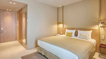 A hotel room with a large bed, a wooden wardrobe, a bedside table with a lamp, and a wall-mounted mirror.