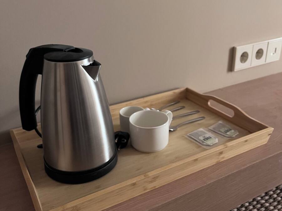 Una tetera de acero inoxidable sobre una bandeja de madera con dos tazas blancas y bolsitas de té.