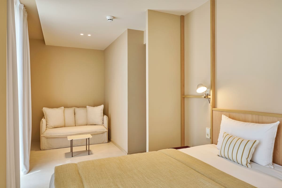 Una habitación de hotel con cama, sofá, mesita de noche y lámpara.