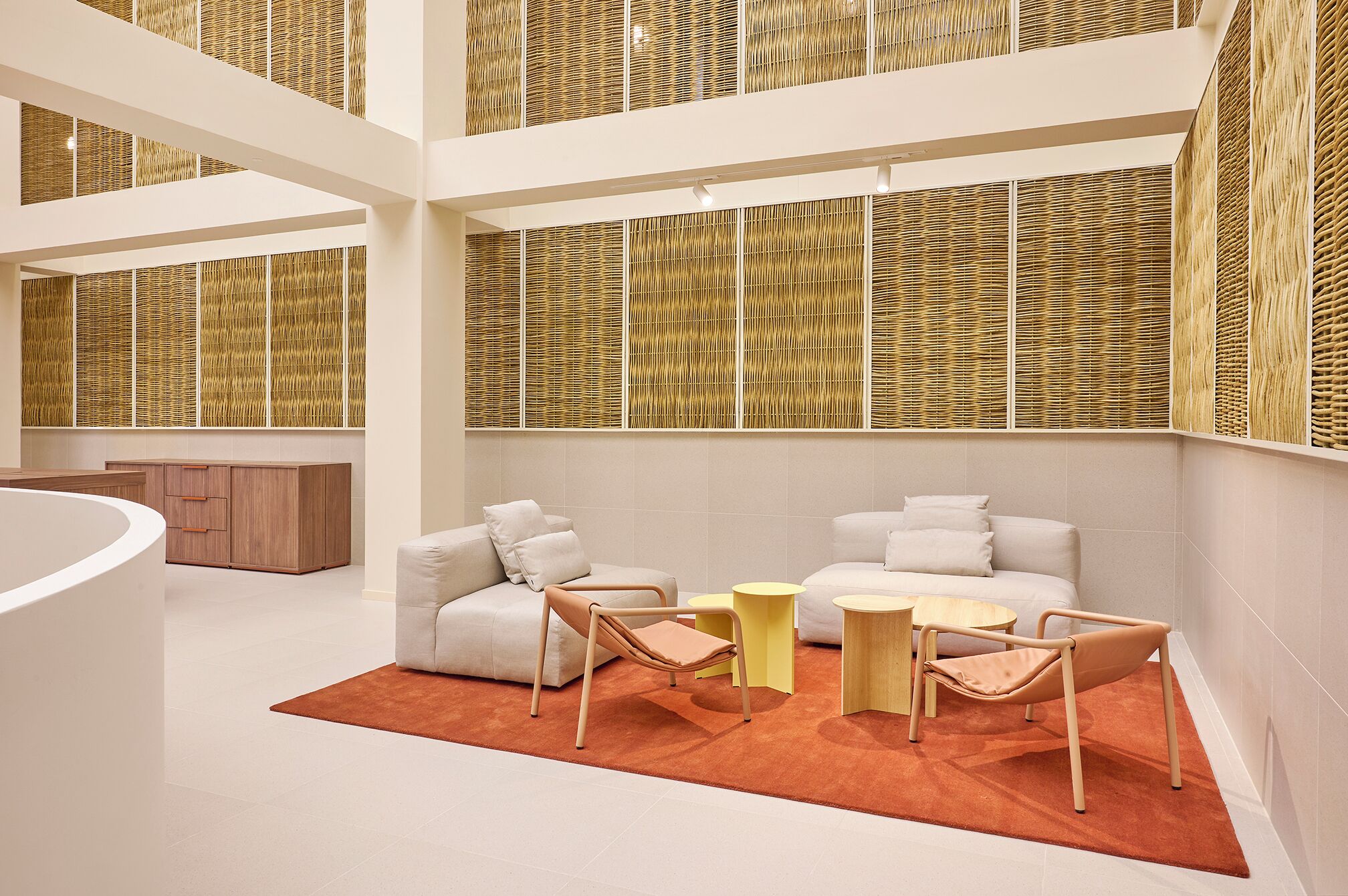 A spacious, modern interior with a central seating area featuring sofas and chairs, a round table, and a curved white structure.