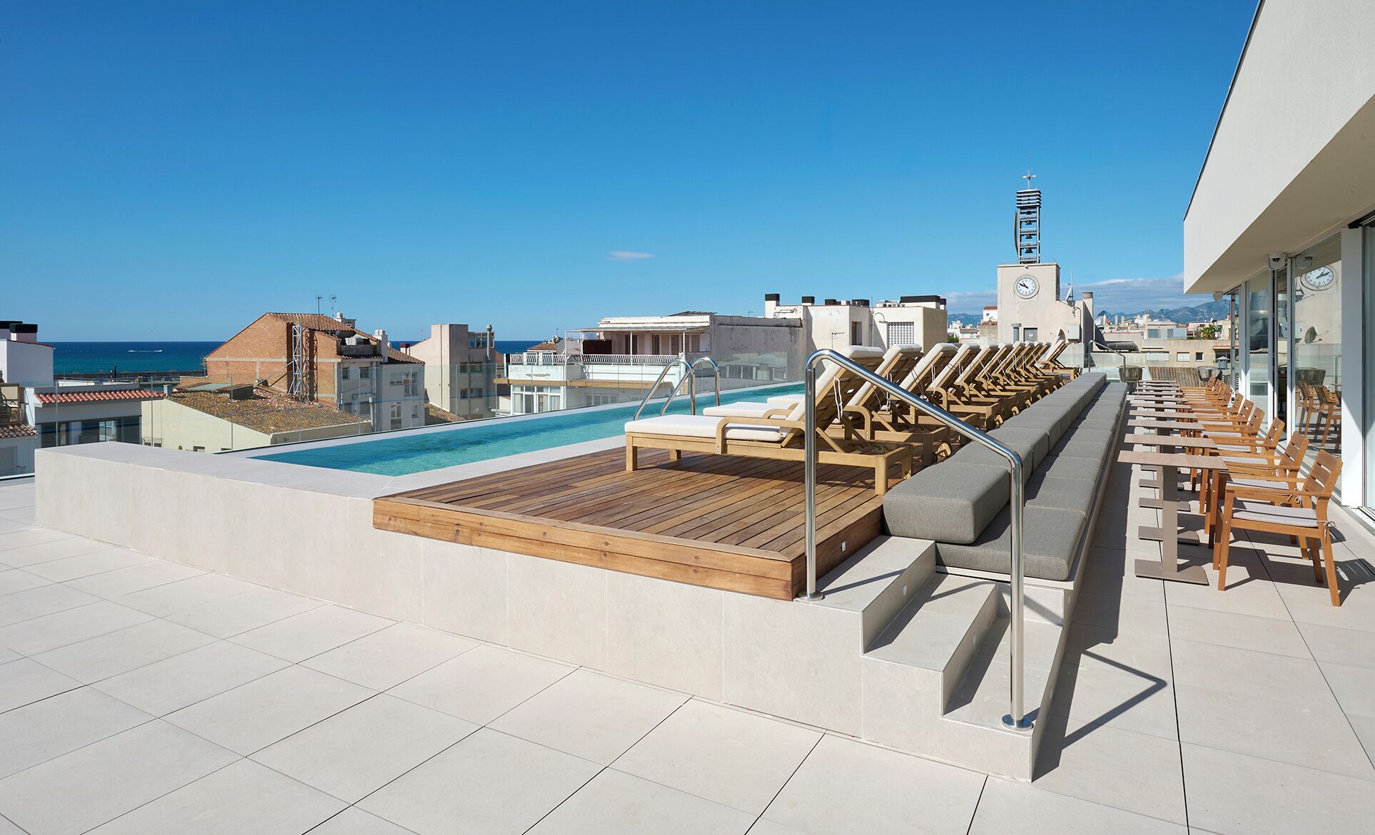 Un espace piscine aménagé sur le toit, avec des chaises longues et une terrasse en bois, offrant une vue sur le paysage urbain et la mer.