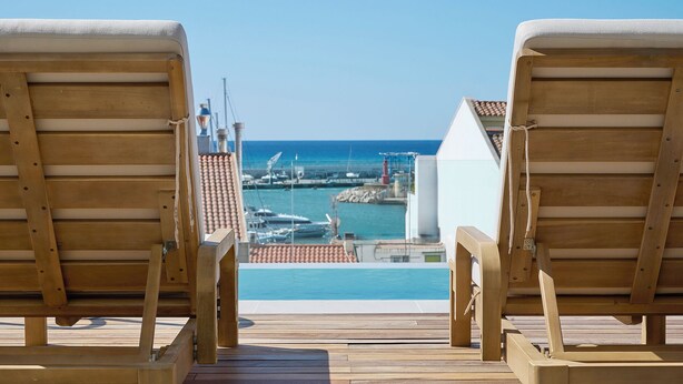 A wooden deck with two lounge chairs facing a pool and marina. - Hotel Marina Cambrils by URH (Cambrils)