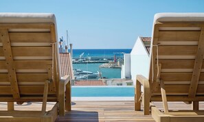 A wooden deck with two lounge chairs facing a pool and marina. - Hotel Marina Cambrils by URH (Cambrils)