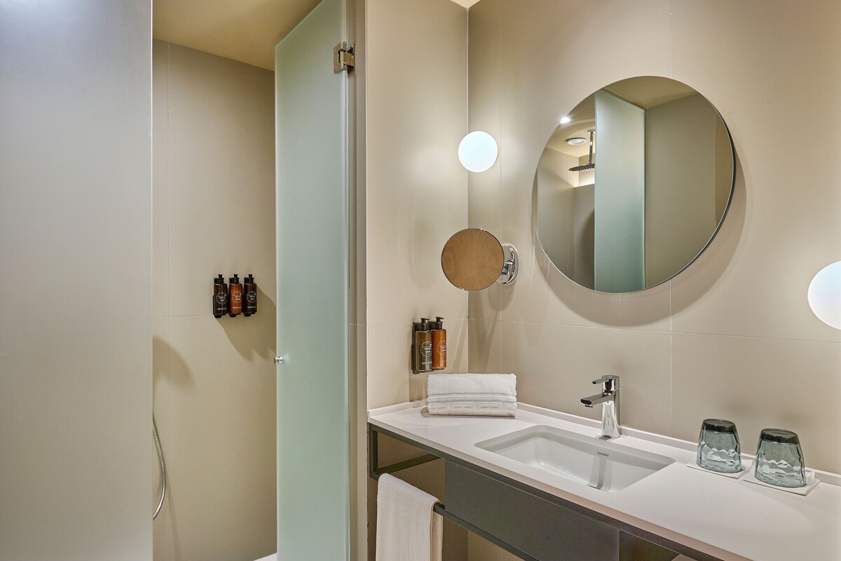 A modern bathroom with a large mirror, two sinks, and a shower.