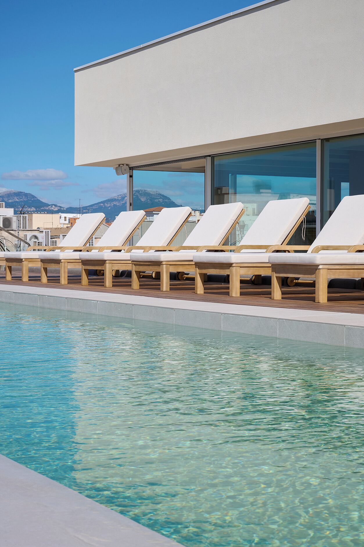 Uma área com espreguiçadeiras à beira da piscina e vista para as montanhas.
