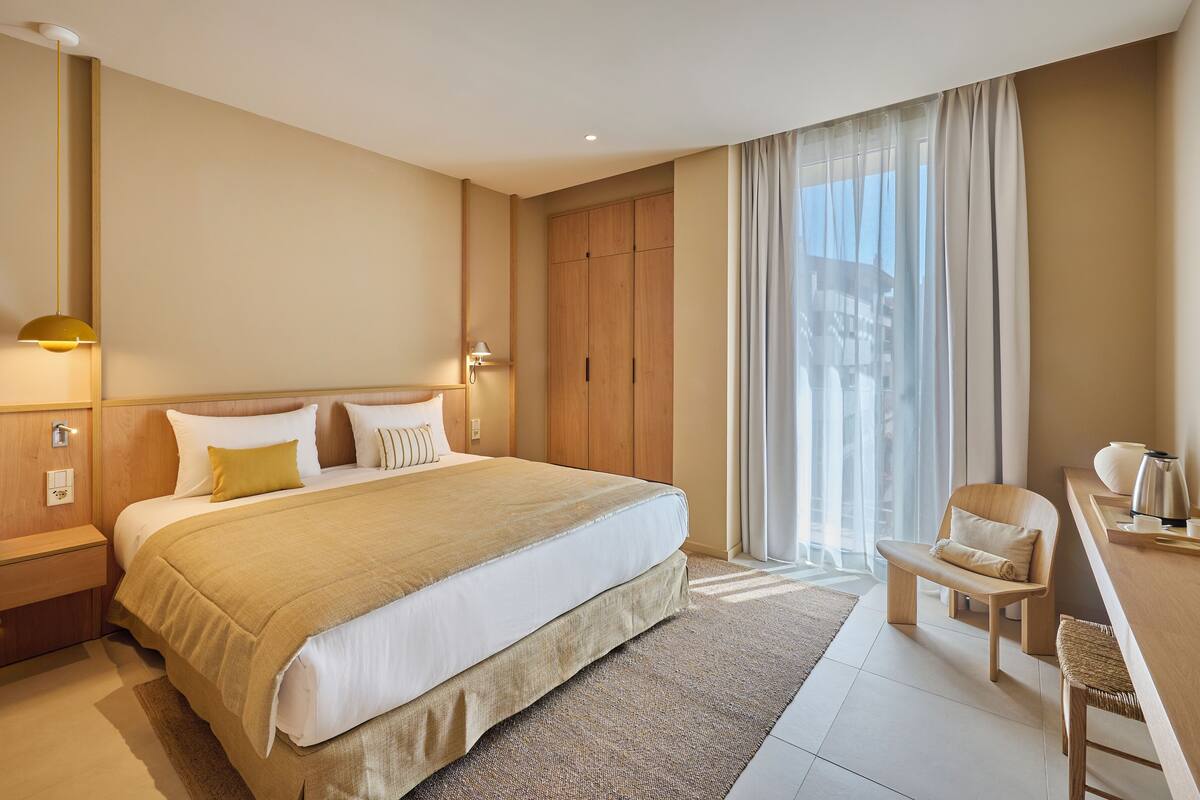 Habitación de hotel con cama, escritorio, silla, armario y una ventana grande con cortinas.