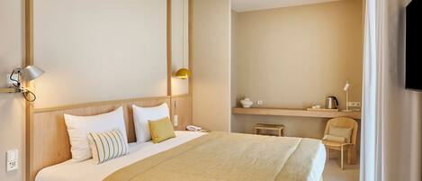 A hotel room with a bed, bedside table, lamp, and a small desk with a chair.