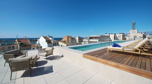 A rooftop pool area with lounge chairs and a view of the sea.