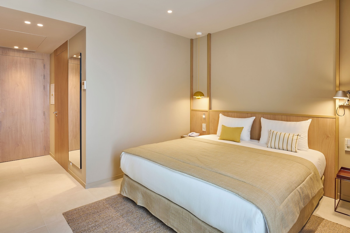 Une chambre d’hôtel avec un lit, une table de chevet, une lampe et une porte.