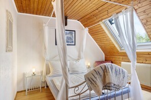 Une chambre à coucher avec un lit à baldaquin, une petite table de chevet avec une lampe, un radiateur et une fenêtre.