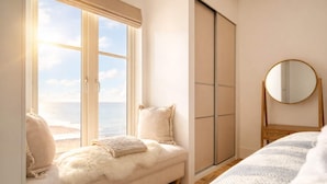 A bedroom with a large window, a bed, a wardrobe, and a mirror.