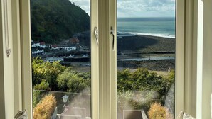 A room with a large window offering a view of a coastal landscape, including a beach and a hill.