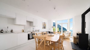 A modern kitchen with white cabinetry, a dining area with wooden chairs, and a large window offering a view of the outdoors.