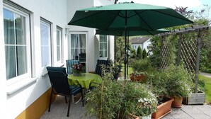 Une terrasse avec une table et des chaises, un parasol vert et des plantes en pot.