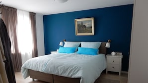 Une chambre à coucher avec un lit, des tables de chevet, un tableau et une fenêtre avec des rideaux.