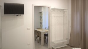 A room with a TV mounted on the wall, a white wardrobe, a desk with a chair, and a shower area with curtains. - REALECASINABORBONICA-INTEGRAL APARTMENT WITH TERRACE IN THE HEART OF PORTICI (Portici)