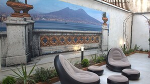 A terrace with outdoor seating, a decorative wall, and a mural of a cityscape with a mountain. - REALECASINABORBONICA-INTEGRAL APARTMENT WITH TERRACE IN THE HEART OF PORTICI (Portici)