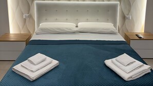 A modern bedroom with a tufted headboard, a teal bedspread, and neatly folded white towels on either side of the bed. - REALECASINABORBONICA-INTEGRAL APARTMENT WITH TERRACE IN THE HEART OF PORTICI (Portici)