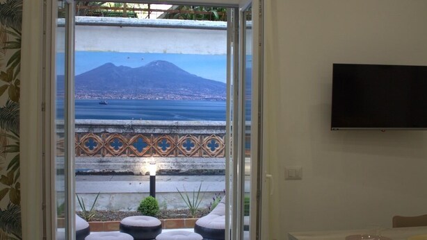 A room with a sliding glass door leading to a balcony with a view of a mountain and water. There is a dining area with a table and chairs. - REALECASINABORBONICA-INTEGRAL APARTMENT WITH TERRACE IN THE HEART OF PORTICI (Portici)