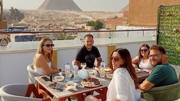 Un grupo de personas cenando al aire libre con una pirámide en el fondo.