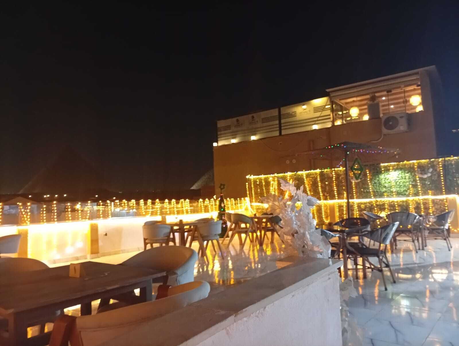 An outdoor seating area with tables and chairs, decorated with string lights and a large illuminated sign.