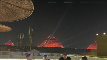 A group of people dining at an outdoor restaurant with a view of a pyramid-shaped building illuminated at night.