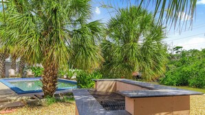 A poolside area with a barbecue grill, palm trees, and a swimming pool.