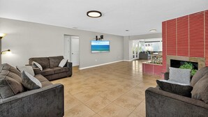 A spacious living room with a fireplace, a flat-screen TV mounted on the wall, and a large window providing natural light.