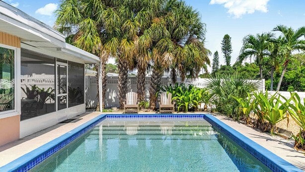 A swimming pool with a blue tiled edge, surrounded by palm trees and a modern house with large windows.