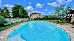 Ein Schwimmbecken mit Steinbord, einer Steinmauer und einem Haus im Hintergrund.