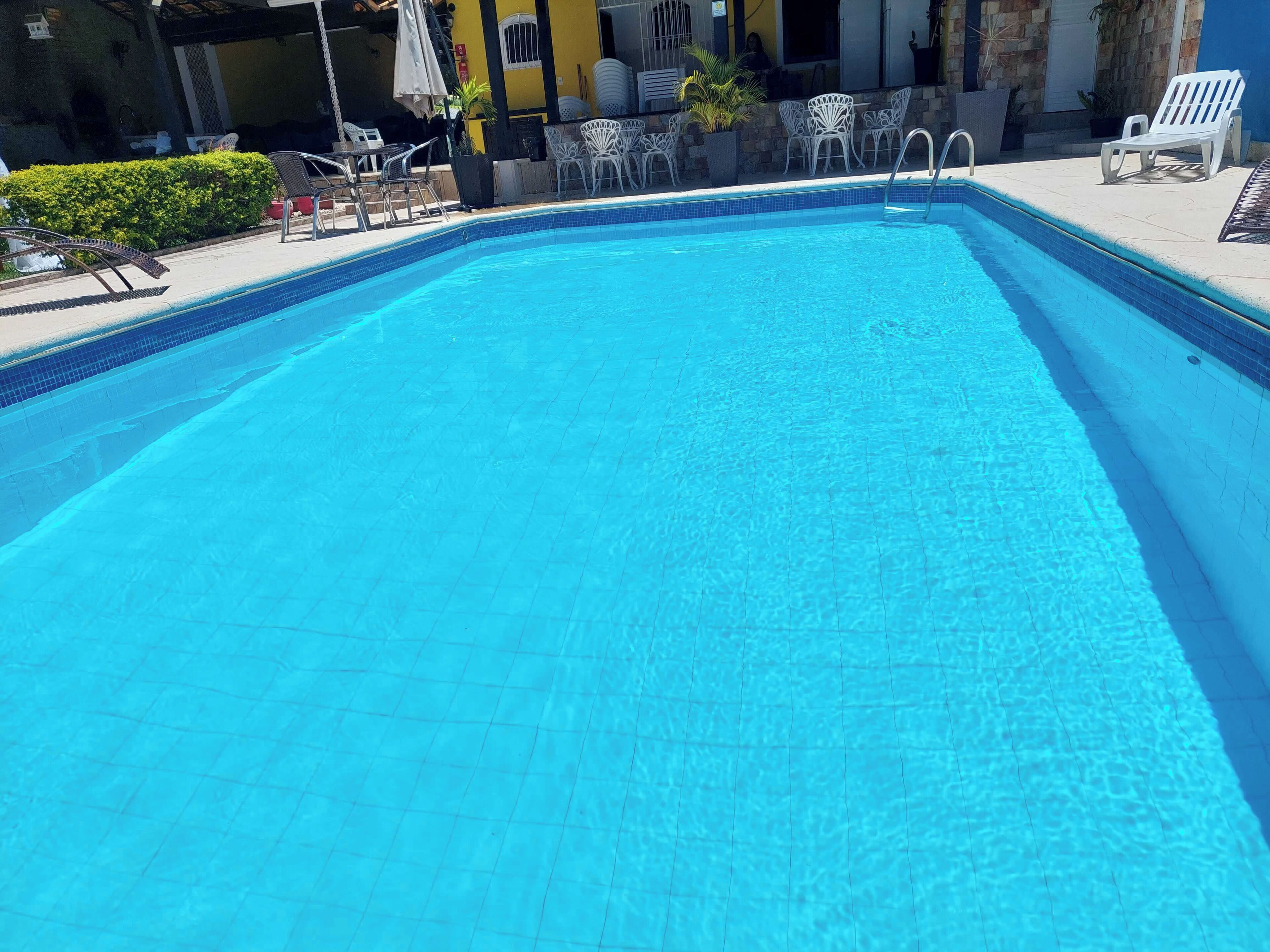 A clear blue pool with white lounge chairs and a stone wall in the background.