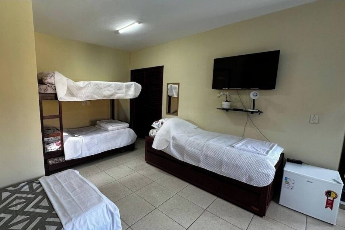 A hotel room with two single beds, a bunk bed, a television, and a refrigerator.