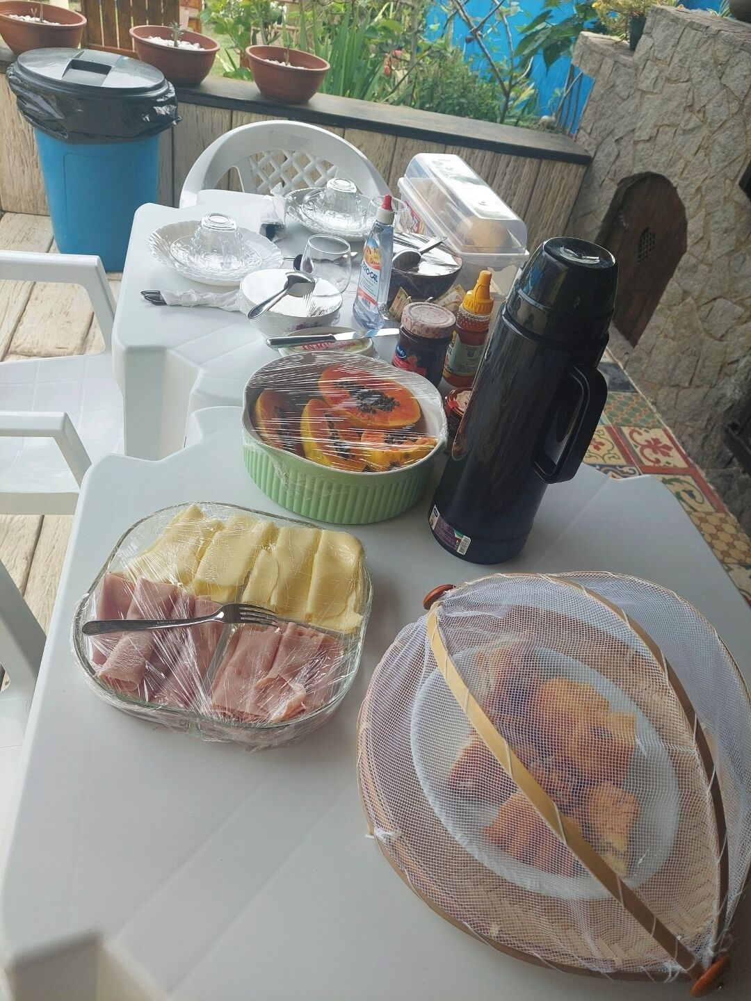 A table set up outdoors with food items, a thermos, and a mesh bag.