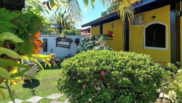 A yellow building with a tiled roof, surrounded by lush greenery and a well-maintained garden. - Pousada Summer Beach by Itaúna (Saquarema)