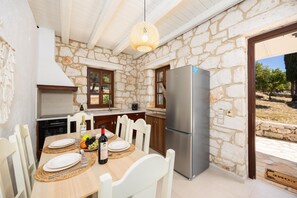 A stone-walled kitchen with a modern stainless steel refrigerator, wooden cabinets, and a dining table set for two.