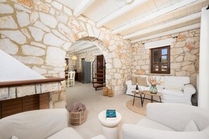 A stone-walled room with a white sofa, a small table with a vase, and a wicker basket.