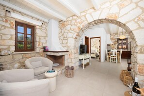 A stone-walled room with a fireplace, a sofa, a dining table, and a television.