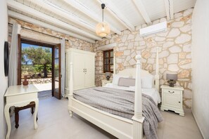 A bedroom with a stone wall, a bed with a white headboard, a bedside table, and a wardrobe.
