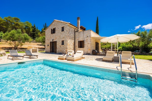 A stone house with a swimming pool, outdoor seating, and a clear blue sky.