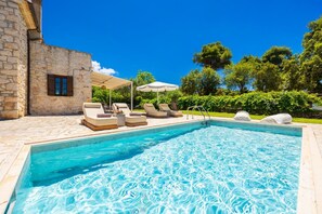A swimming pool with lounge chairs, a stone building, and a clear blue sky.