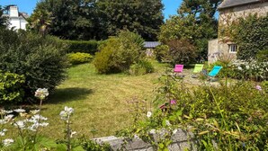 Un jardín con césped, diversas plantas y algunas sillas de exterior.
