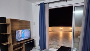 A modern living room with a flat-screen TV on a wooden stand, a glass door leading to an outdoor area with a tiled floor, and a small table with a black top. - Fully Equipped Rooftop house with private terrace in Beau Bois, St-Pierre, Moka (Saint Pierre)