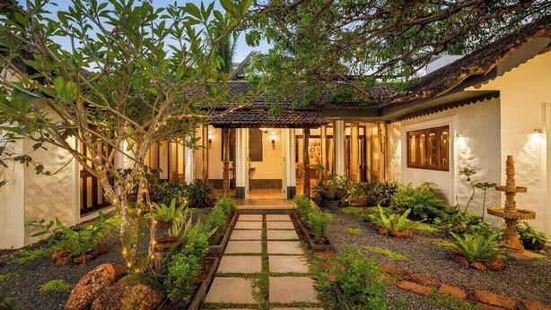 Un edificio tradizionale con tetto in tegole, un vialetto in pietra che conduce all'ingresso e diverse piante e rocce nel giardino.
