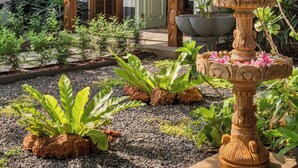 Una casa tradizionale con tetto in tegole, un giardino con fontana in pietra e diverse piante.