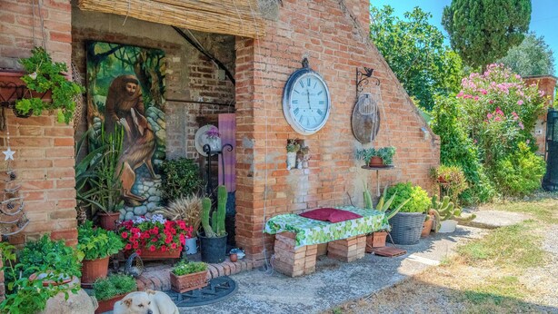 A rustic brick building with a mural, a clock, and various potted plants. - Casa di Cristina - Tra Montepulciano e il Lago Trasimeno (Casamaggiore)