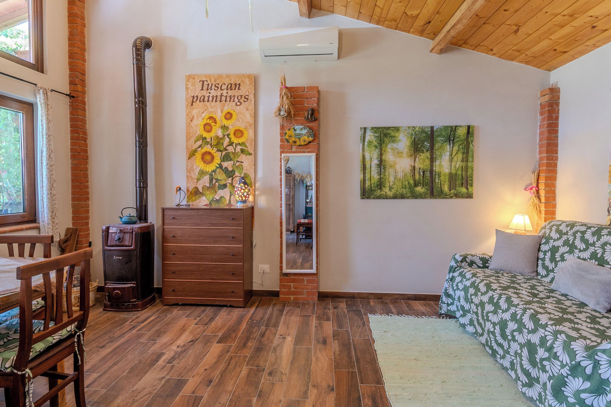 Um quarto aconchegante com piso de madeira, um sofá, um penteou e um quadro de girassóis.